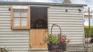 A rustic wooden house with a wooden door and window, a wooden bench, and a flower pot on the porch. - This cosy and quiet Shepherd’s Hut is a great way to unwind. (Frampton-on-Severn)