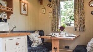 A cozy room with a wooden bench, a small table with a vase of flowers, and a window with floral curtains. - This cosy and quiet Shepherd’s Hut is a great way to unwind. (Frampton-on-Severn)