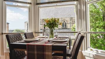 A dining area with a table set for four, large windows with blinds, and a view of a building with a pointed arch window.