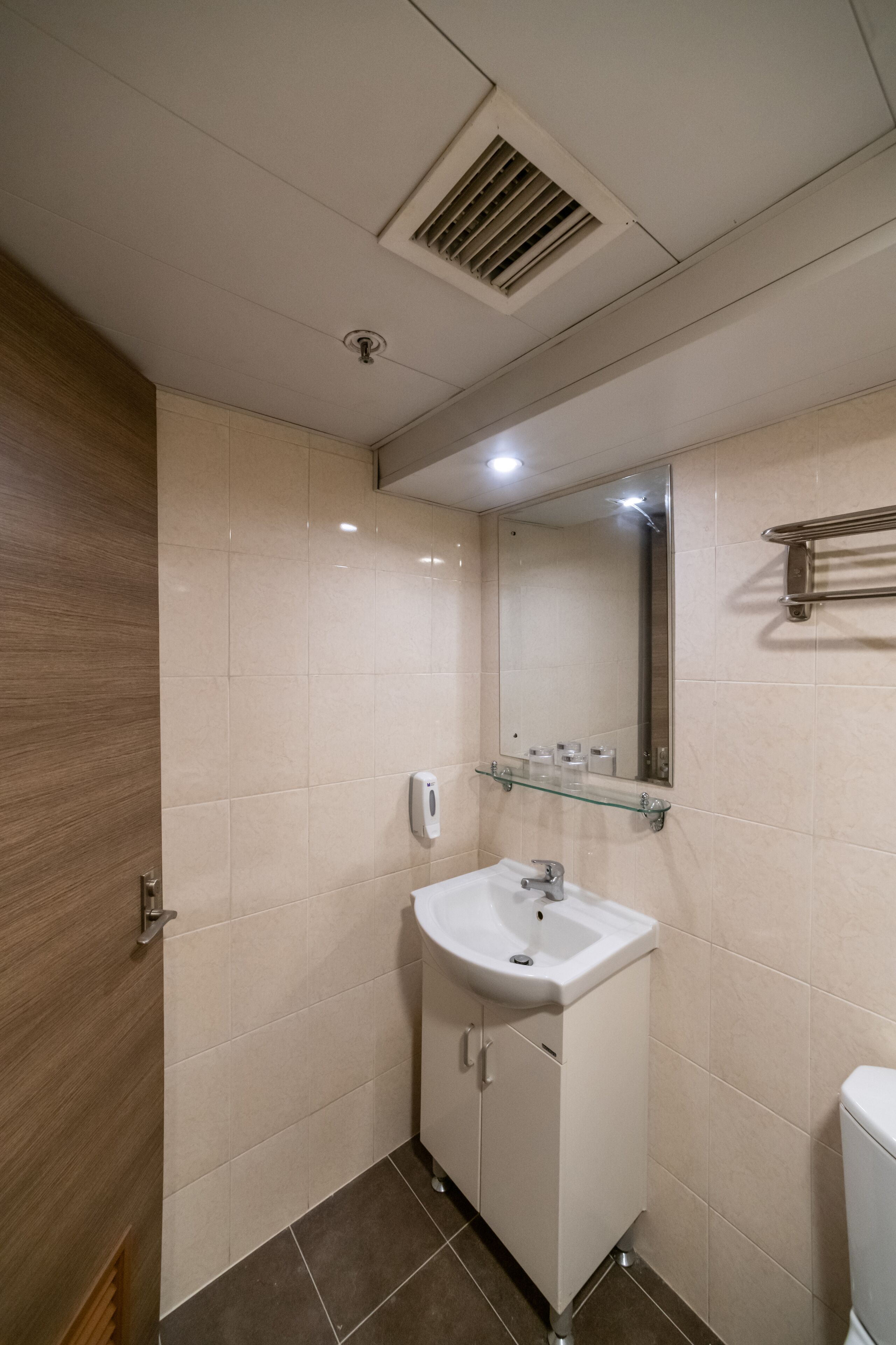 A modern bathroom with a white sink, mirror, and beige tiles.