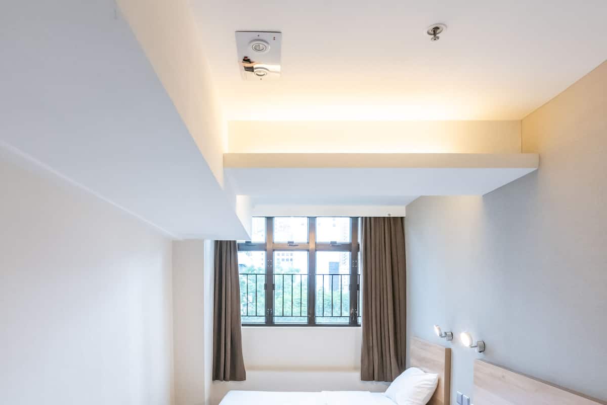 A hotel room with two beds, a window with curtains, a ceiling light, and a wall-mounted phone.