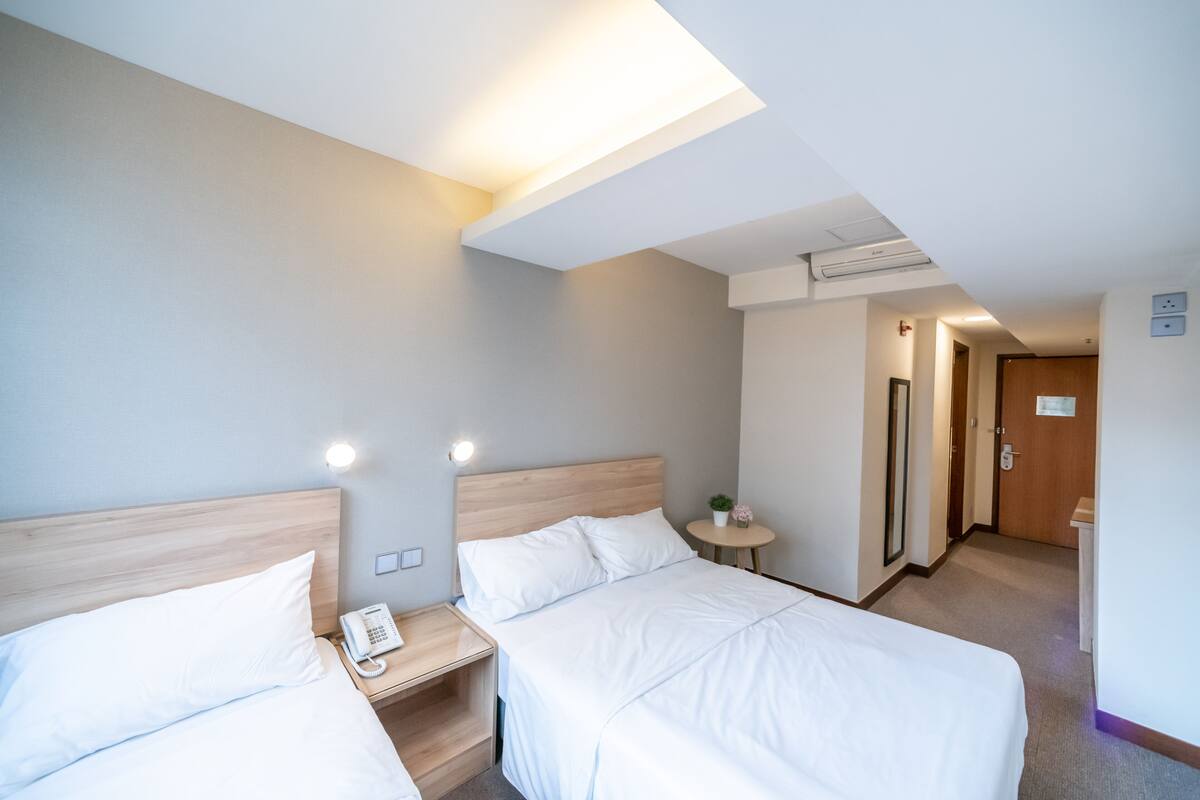 A hotel room with two beds, bedside tables, a phone, a small table with a plant, and a door leading to another room.