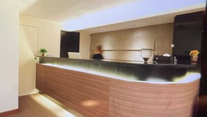 A reception area with a curved reception desk, a potted plant, and a wall-mounted TV. - metacity living (Kowloon)