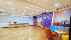 A spacious room with a wooden floor, a bench, a blue sofa, and a small table with a vase. - metacity living (Kowloon)