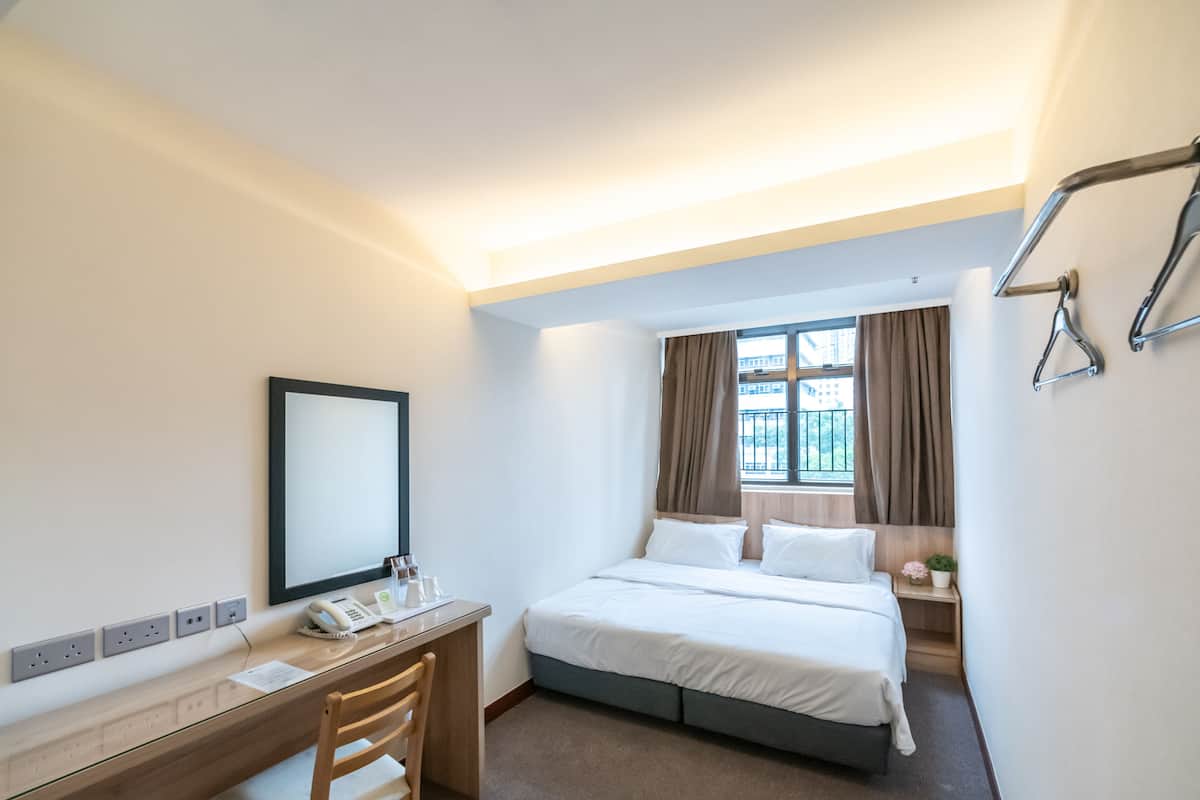 A hotel room with a bed, desk, chair, and a window with curtains.