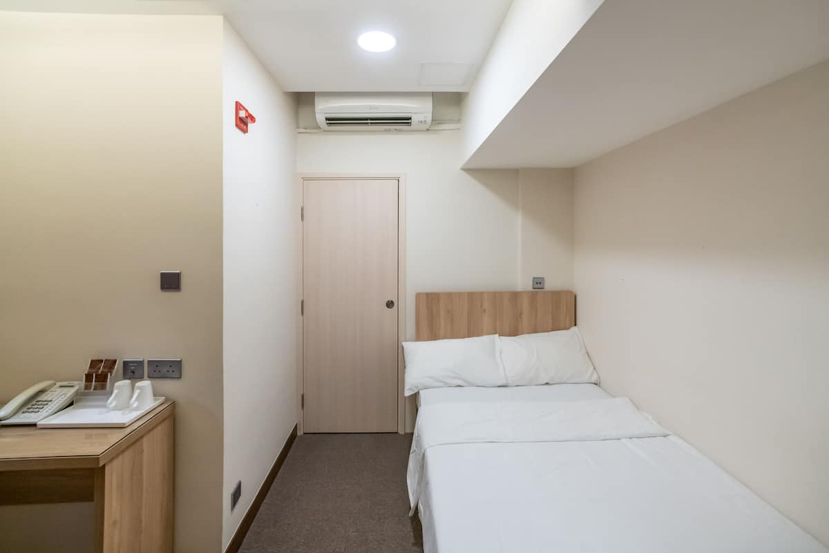A hotel room with a bed, a desk with a telephone, and an air conditioning unit.