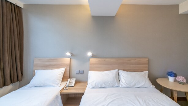 A hotel room with two beds, a bedside table with a phone, and a small round table with a vase of flowers. - metacity living (Kowloon)