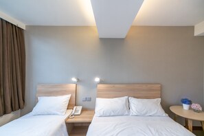 A hotel room with two beds, a bedside table with a phone, and a small round table with a vase of flowers. - metacity living (Kowloon)