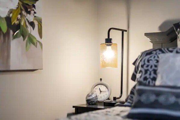A bedside table with a clock, a decorative item, and a wall-mounted lamp. - Fall Special! Close to Everything, remodeled 3 bdrm house, large deck (Marietta)
