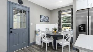 A modern kitchen with a grey door, white chairs, a round table, and a stainless steel refrigerator.