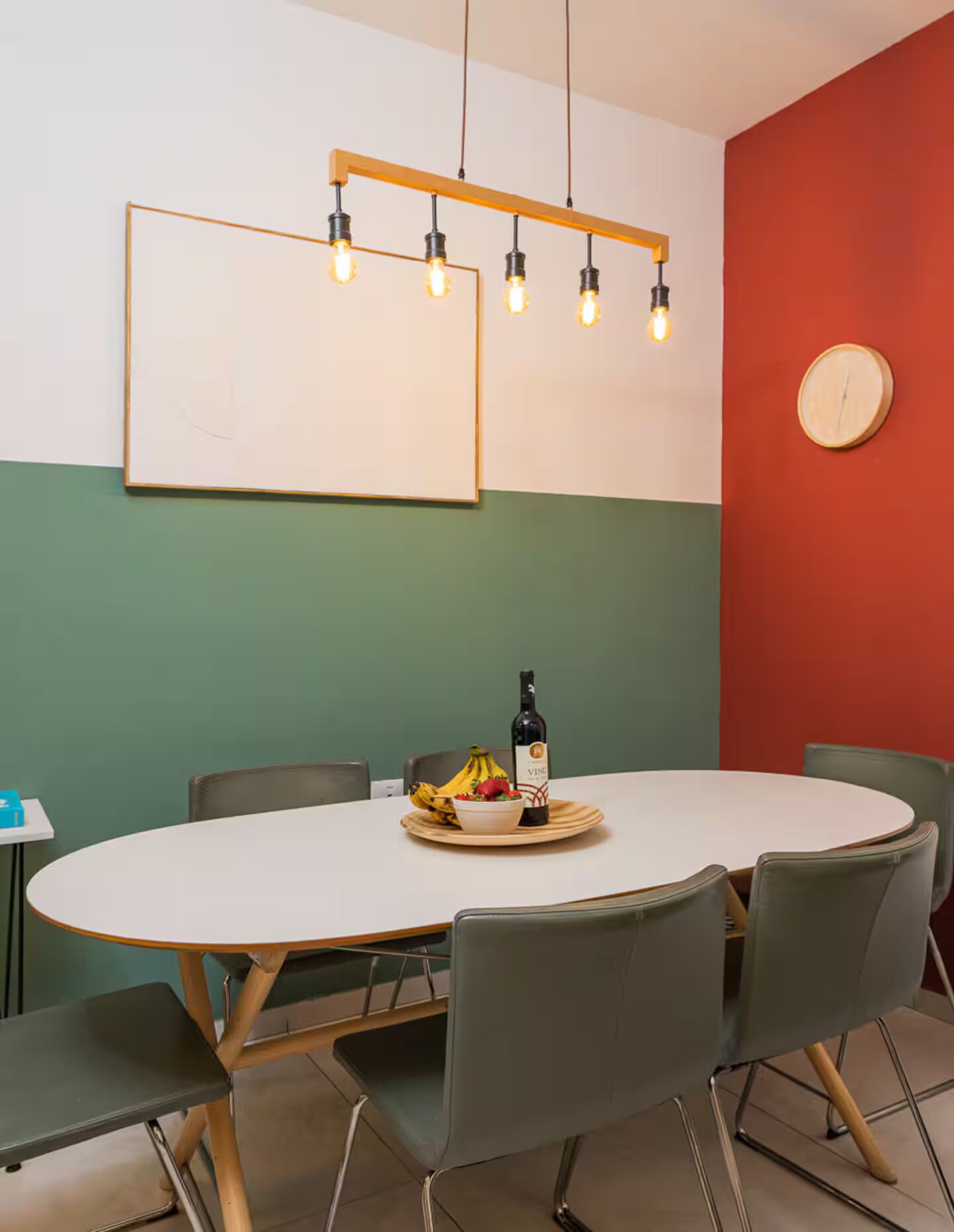 Een vergaderruimte met een ronde tafel, stoelen, een klok en een fles wijn.
