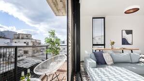 A modern living room with a sofa, a dining table, and a balcony with white chairs and a potted plant. - CARMEL MARKET - Exclusive Collection - By HOMY (Tel Aviv)