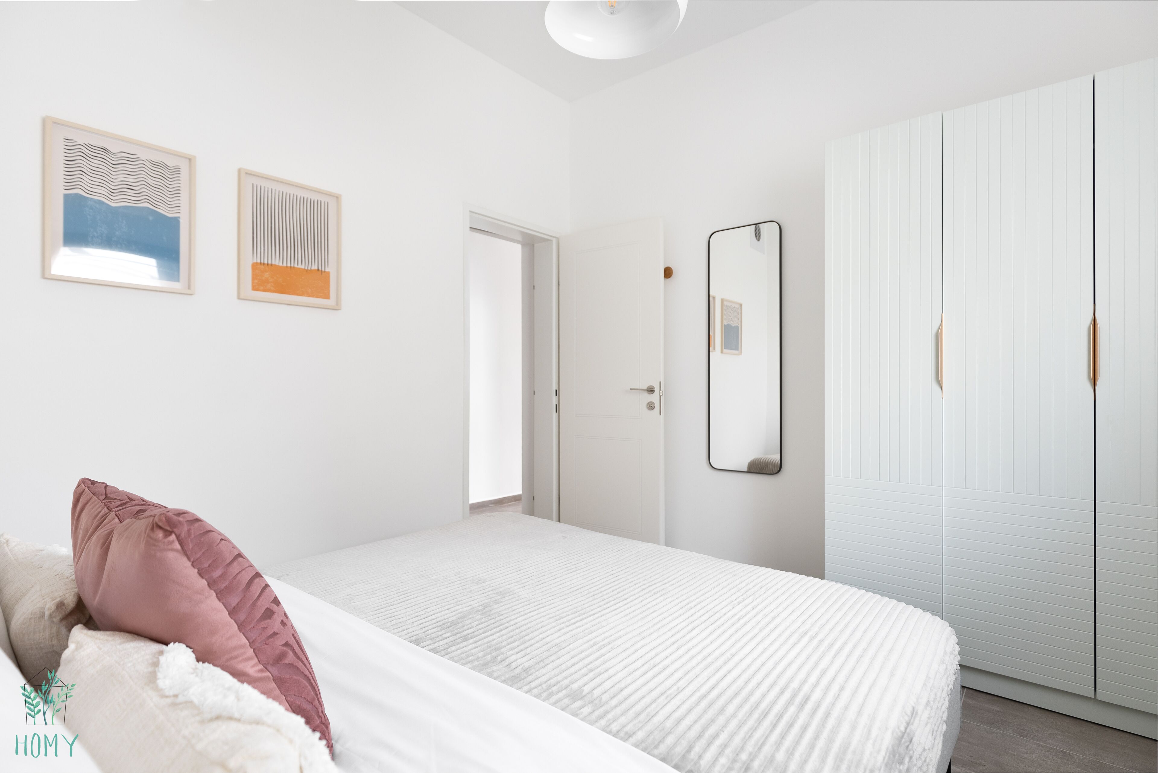 A bedroom with a bed, a wardrobe, and two framed artworks on the wall.