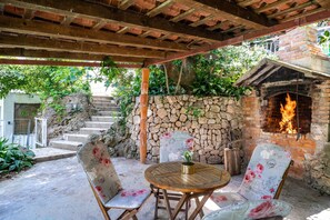 Un patio al aire libre con un muro de piedra, una chimenea de ladrillo con fuego, y sillas y mesa con estampado floral.