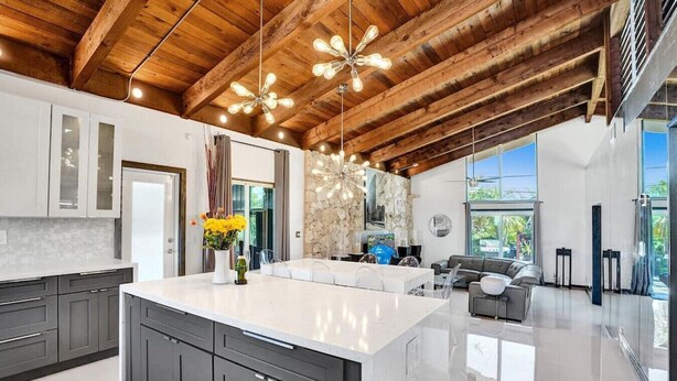 A modern kitchen with a large island, dark cabinetry, and a stone accent wall. - Mid-Century Chic | Pool & Hot Tub | Skyview Loft (Fort Lauderdale)