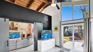 A modern living room with a stone wall, a pool view, a white sofa, and a large window overlooking a patio. - Mid-Century Chic | Pool & Hot Tub | Skyview Loft (Fort Lauderdale)