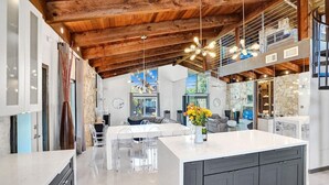 A modern kitchen with a large island, wooden ceiling beams, and a view to the living area. - Mid-Century Chic | Pool & Hot Tub | Skyview Loft (Fort Lauderdale)