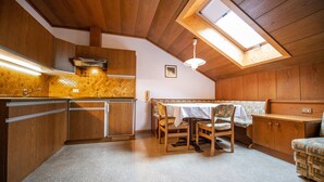 A compact kitchen with wooden cabinets, a dining table with chairs, and a skylight. - 302A Apartments Garni Zilli (Laion)