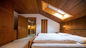 A bedroom with a wooden ceiling, a skylight, a bed with white bedding, and wooden walls. - 302A Apartments Garni Zilli (Laion)