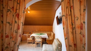 A cozy room with a wooden ceiling, a bench, a table with a green tablecloth, and floral curtains.
