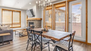 Amplio salón con una gran mesa de comedor de madera, asientos cómodos, chimenea de piedra y ventanas grandes con persianas de madera.