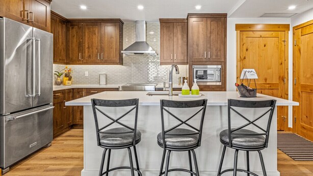 Una cocina moderna con armarios de madera, un refrigerador de acero inoxidable, una isla central con taburetes de bar y un microondas.