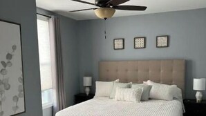 A bedroom with a bed, a ceiling fan, and framed artwork on the wall. - Central House
Home Away From Home! (Bluffton)