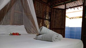 A bed with white linens and a rolled towel, a mosquito net, and a view of a blue-tiled wall. - Las Palmeras (Rosario Islands)