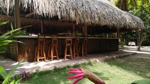 A thatched-roof structure with wooden chairs and a table, surrounded by greenery. - Las Palmeras (Rosario Islands)