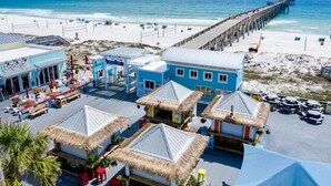 A beachside resort with thatched-roof huts, a pier, and a beachfront bar.