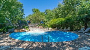 Una piscina circular con borde de piedra, rodeada de sillas de descanso y una terraza de madera.