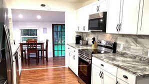 A modern kitchen with white cabinets, stainless steel appliances, and a wooden floor.
