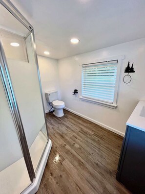 Ein Badezimmer mit Dusche, Toilette und einem Fenster mit Jalousien.