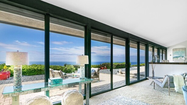 A modern interior with large glass windows, a glass table, and a view of the ocean.