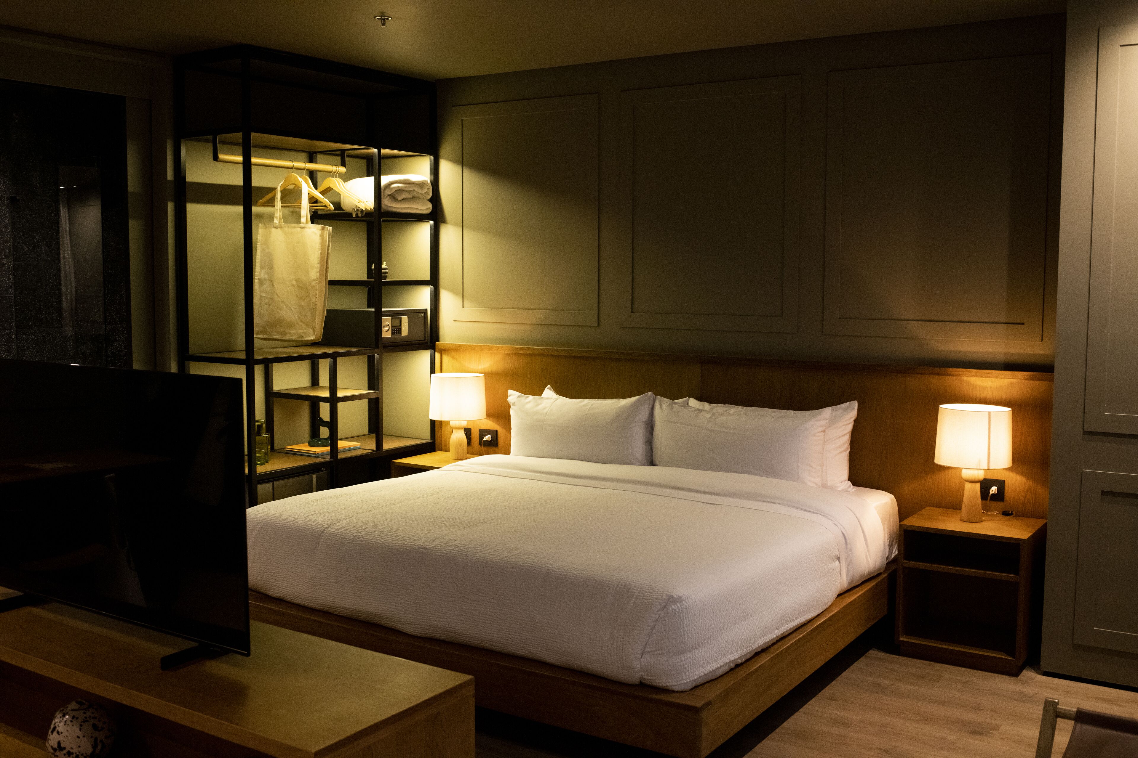 Une chambre d’hôtel avec un grand lit, deux tables de chevet avec des lampes, un téléviseur posé sur un meuble et une armoire avec des étagères.