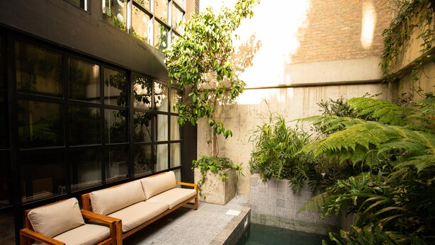A modern outdoor seating area with a pool, surrounded by lush greenery and a brick wall. - Hotel Coco (Bogotá)