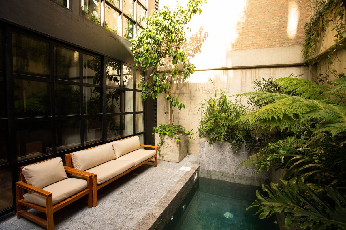 Uma área de estar moderna ao ar livre, com piscina, cercada por vegetação exuberante e um muro de tijolos.
