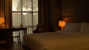 Una habitación de hotel con una cama grande, dos lámparas de noche, un escritorio con una silla y una ventana con cortinas ligeras.