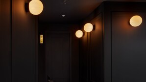A hallway with a red carpet, black walls, and three round wall-mounted lights. - Hotel Coco (Bogotá)