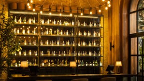 A bar area with multiple shelves of bottles, a curved light fixture, and several seating arrangements. - Hotel Coco (Bogotá)