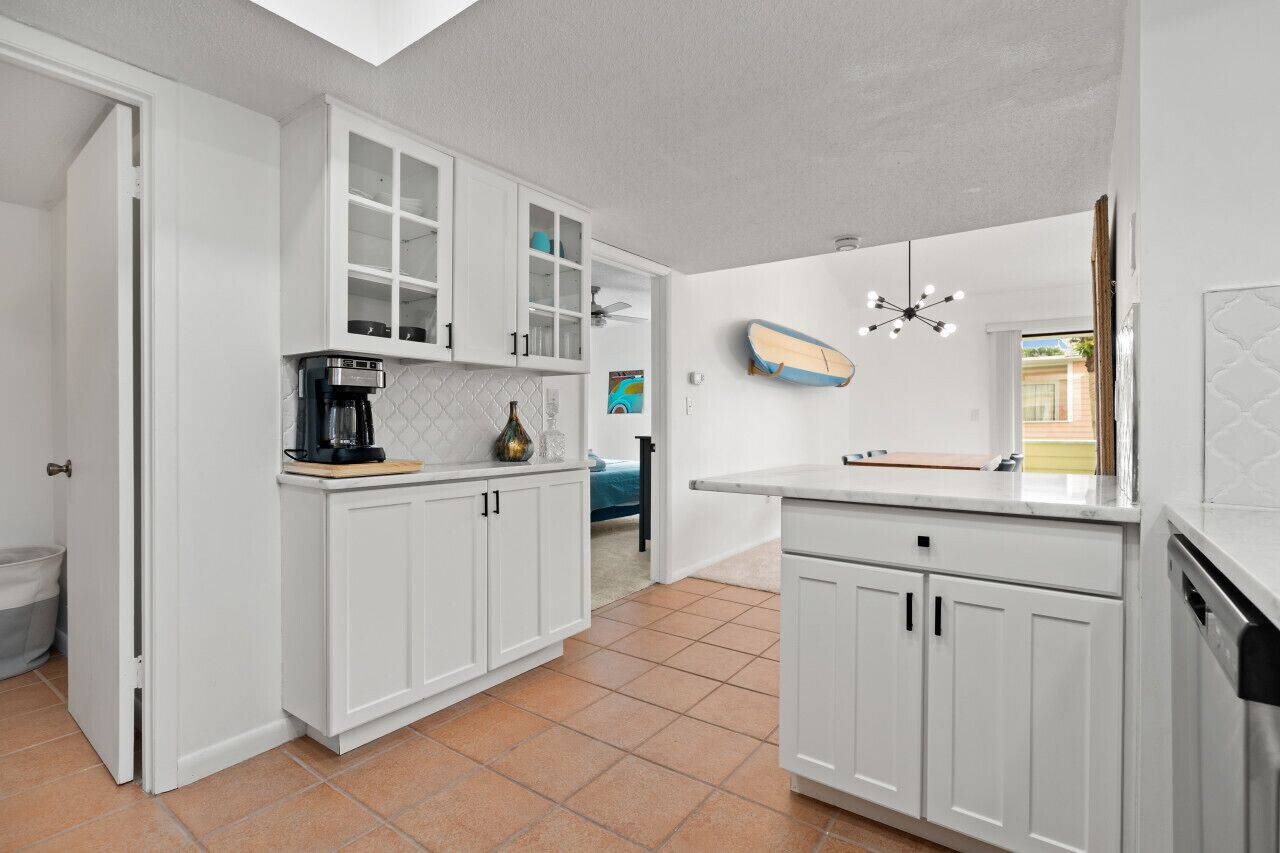 A kitchen with white cabinets, a coffee maker, and a surfboard on the wall.