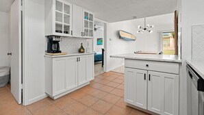 Eine Küche mit weißen Schränken, einer Kaffeemaschine und einem Surfbrett an der Wand.