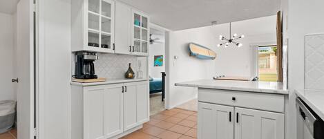 A kitchen with white cabinets, a coffee maker, and a surfboard on the wall.