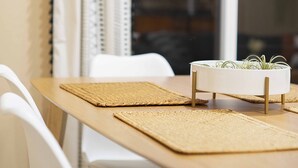 A dining table with a woven placemat, white chairs, and a white planter with plants.