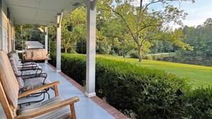 A covered porch with outdoor seating and a view of a manicured lawn and trees. - Pond House on the Plains, Auburn, Firetruck rides (Opelika)
