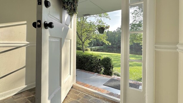 A white door with a doorknob and a small window, leading to a covered porch with a view of a well-maintained lawn and trees. - Pond House on the Plains, Auburn, Firetruck rides (Opelika)