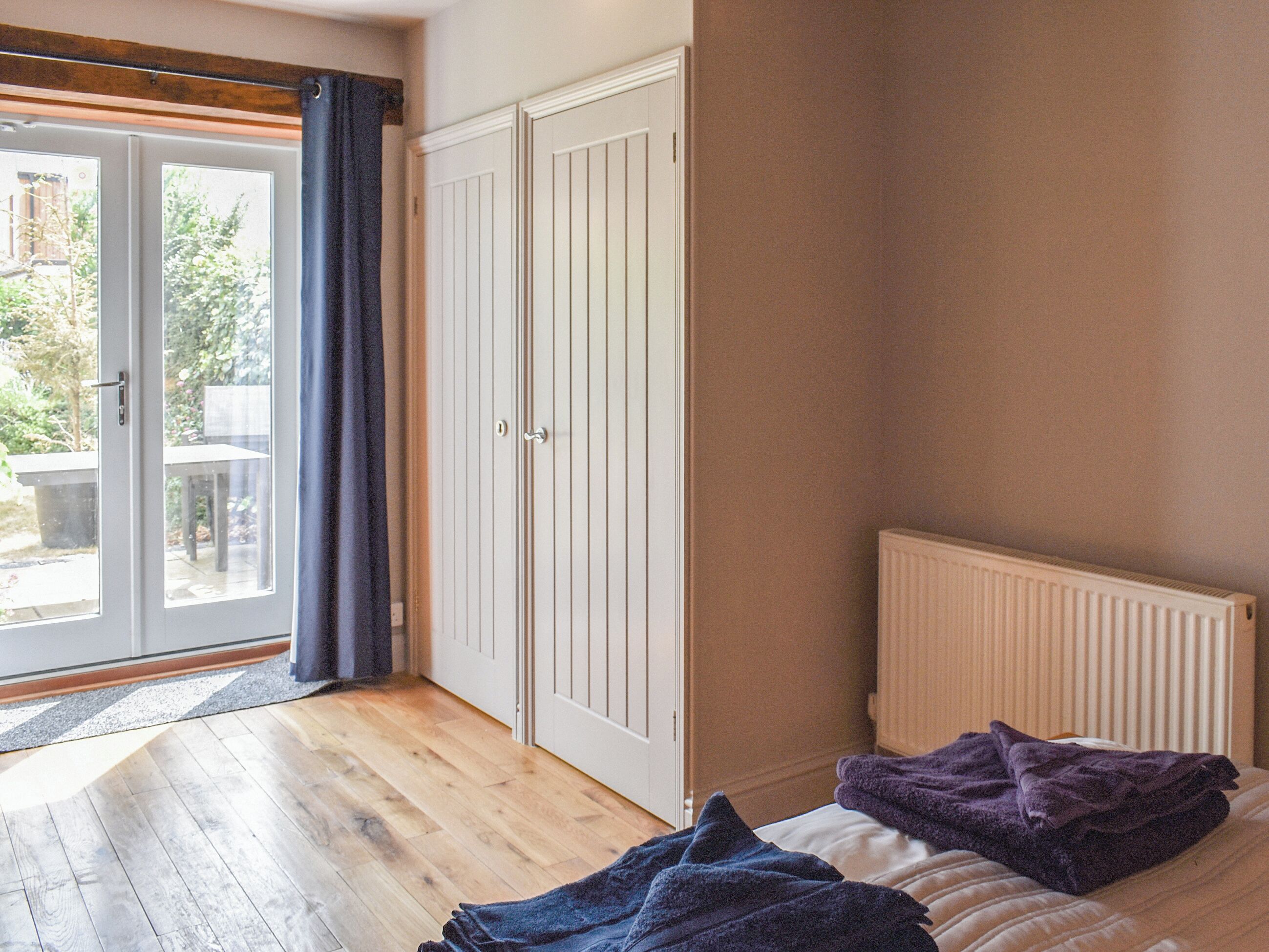 Une chambre avec un lit, un radiateur, une armoire et une porte-fenêtre coulissante donnant sur l’extérieur.