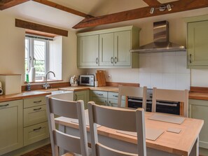 A kitchen with wooden beams, a sink, a microwave, cabinets, and a dining table with chairs.
