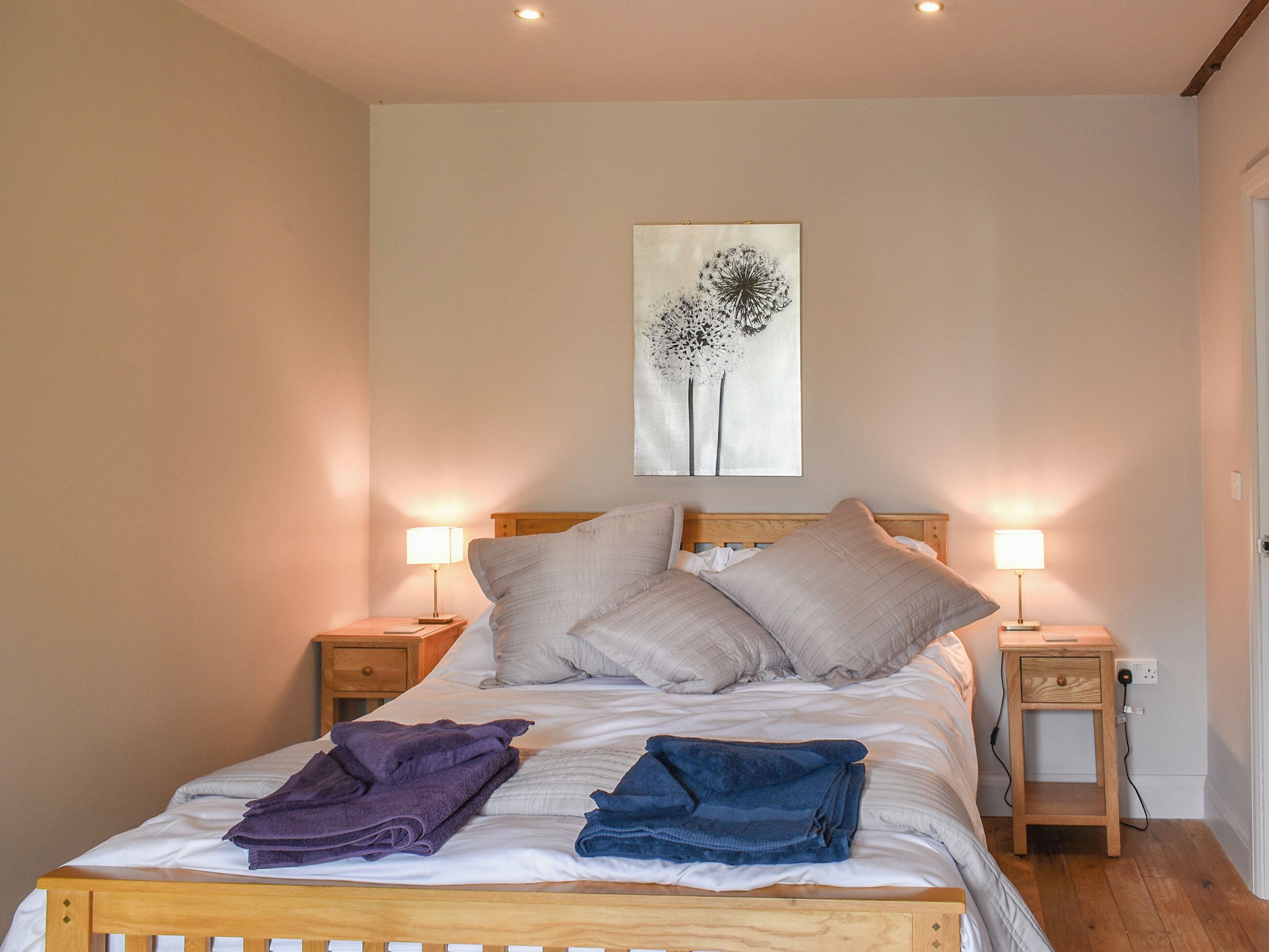 A neatly made bed with pillows, a bedside table with a lamp, and a wall art piece.