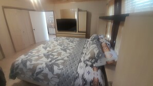 Ein Schlafzimmer mit Bett, Fernseher, Kleiderschrank und Fenster.